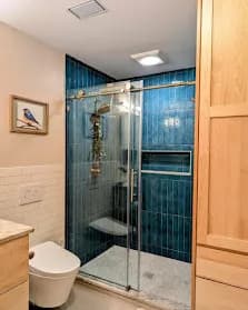 Vertical deep-blue subway-tile shower with frameless glass and marble pebble pan.