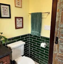 Same project, different angle: green tile half-wall, framed butterfly prints on the yellow wall, sage towel.