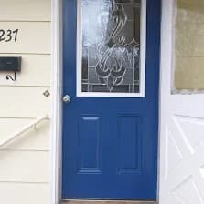 The dark teal blue front entry door Peggy Lindner picked, installed on a brick home with white-painted brick surround.