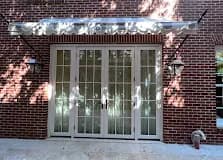 White-framed exterior French entry on a brick home with flanking sconces.