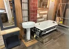 Cast-iron tubs, pedestal sinks, the unusual pieces. Staged against brick and reclaimed wood.