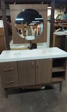 Single light-wood vanity, round mirror, white quartz top, slender legs. One of several vanities staged so you can see real proportions.