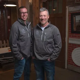 A photo of Josh inside the showroom, in a grey Price-Less zip jacket with the circular logo on the chest.